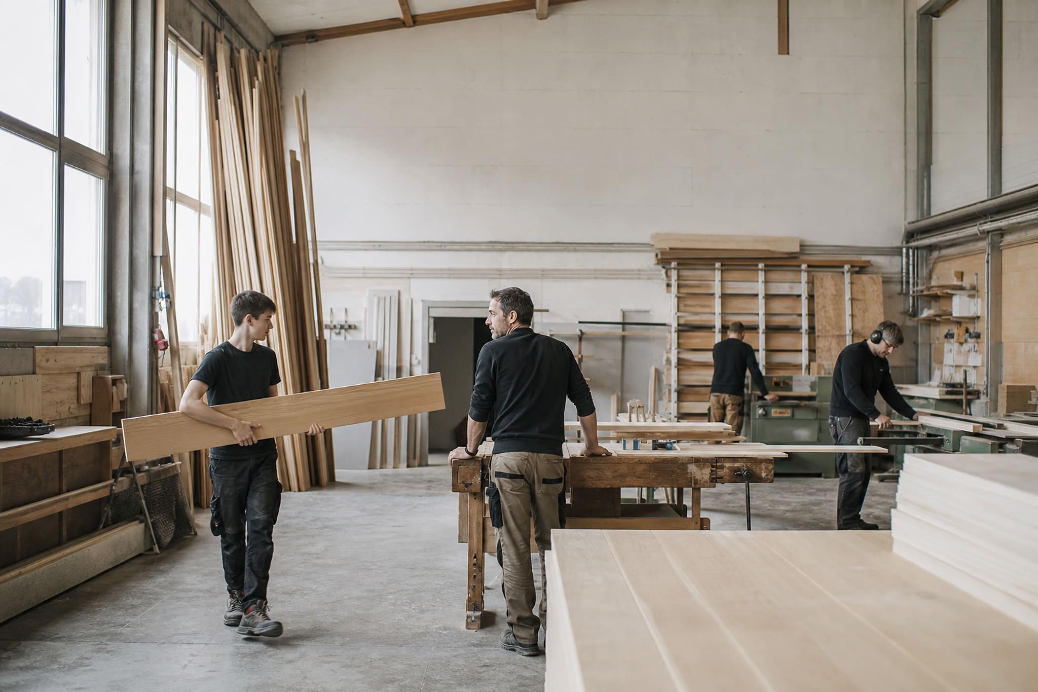 Vier Personen arbeiten in der hellen Werkstatt eines Schreinereibetriebs.